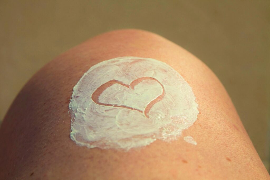 Een knie met daarop een witte crème, waarin een hartje getekend is. 