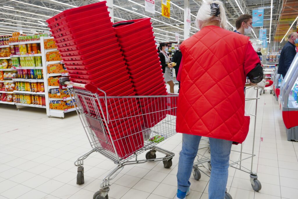 Droge voeding, kassa 4 - een volle winkelkar, gevuld met rode winkelmandjes. Daarnaast staat een oudere dame met een rode jas. 