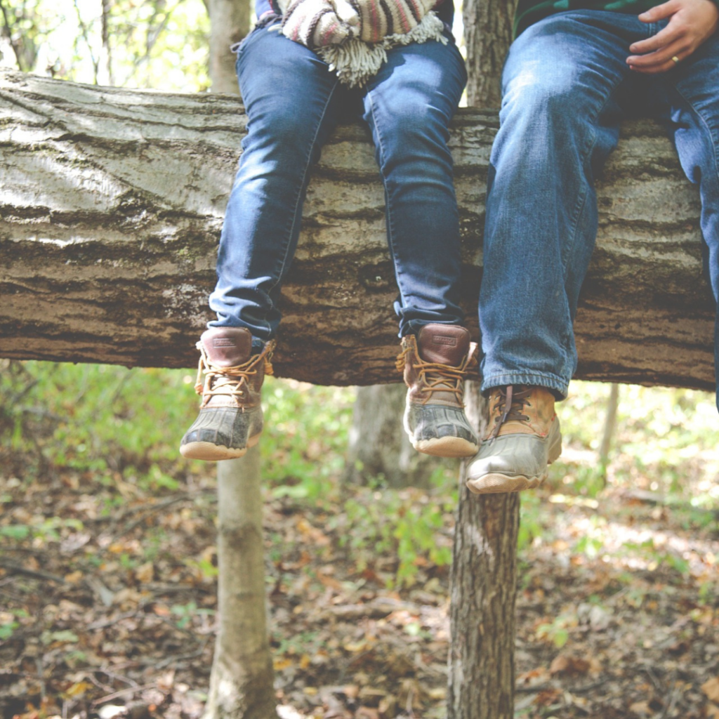 niet zo met bezig met kledij: de benen van een man en een vrouw, zittend op een boomstronk. Allebei dragen ze een gemakkelijk zittende broek en comfortabele schoenen 