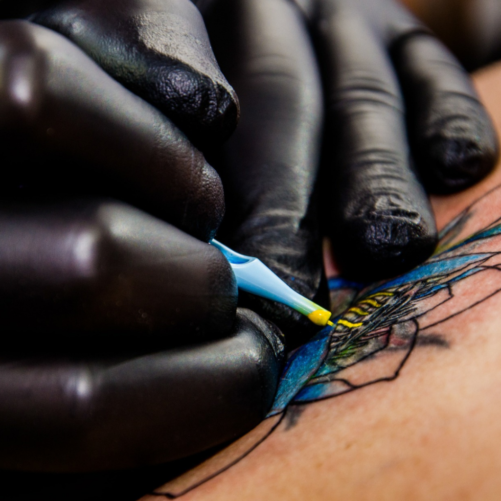 een stoer watje: hand van een tatoo-artiest die een watercolor tattoo plaatst