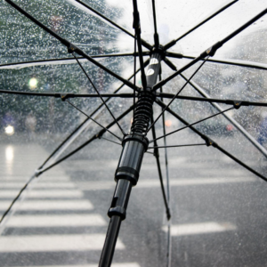 De donkere dagen door: een transparante paraplu met regendruppels op. Door de paraplu zie je een zebrapad. 