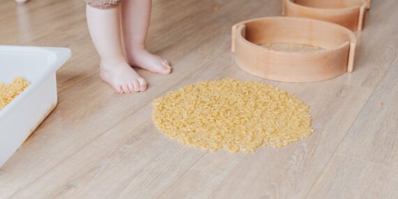 anonymous toddler developing fine motor skills while playing with wooden shapes and pasta at home